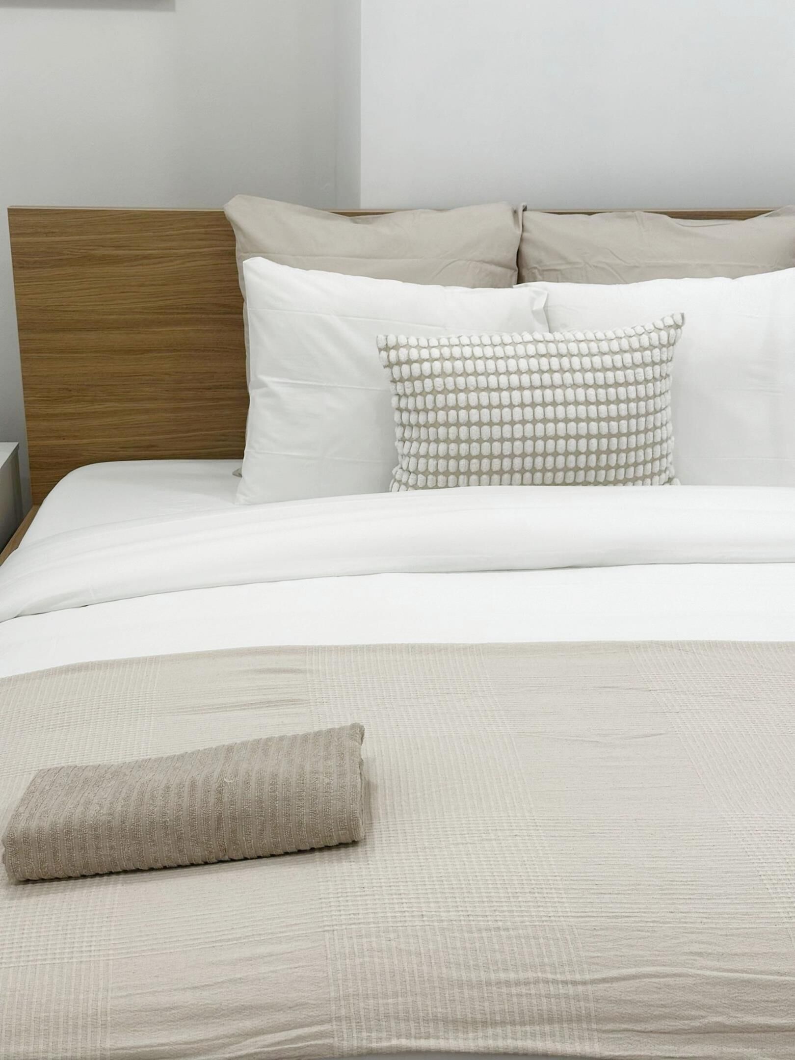 Una cama bien tendida con cabecera de madera, ropa de cama blanca y una almohada decorativa.