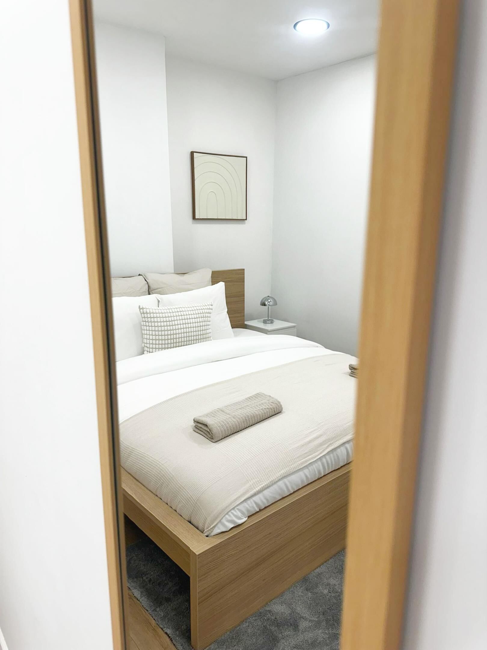 A neatly made bed with a wooden frame, a bedside table with a lamp, and a framed picture on the wall.