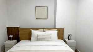 Una cama bien tendida con dos almohadas, un cabecero y una mesita de noche con una lámpara.