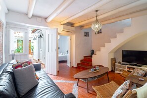 Ein modernes Wohnzimmer mit Sofa, Couchtisch und Korbstühlen. Eine Treppe führt zu einer oberen Ebene, ein Flachbildfernseher und ein Essbereich sind ebenfalls vorhanden.