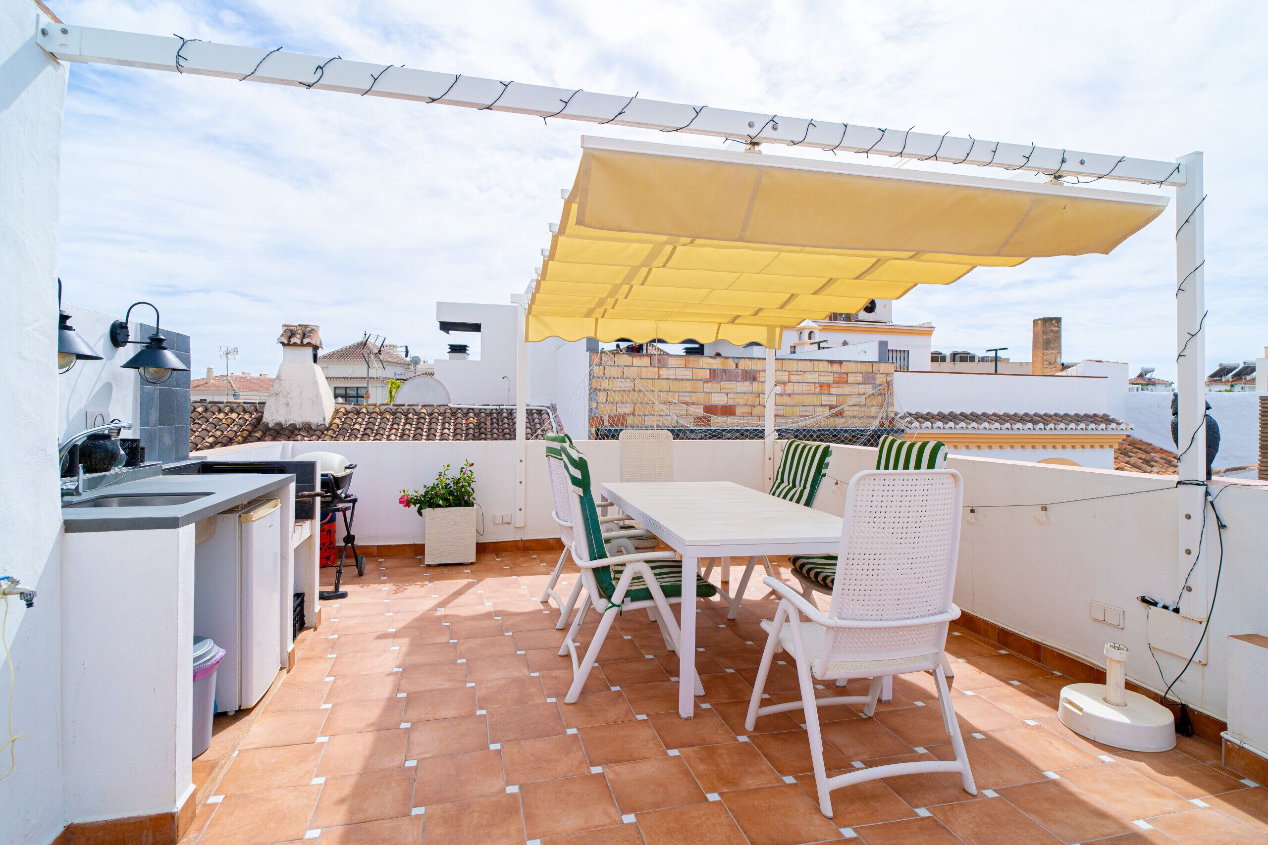 Una terraza en la azotea con zona de comedor, cocina al aire libre y un toldo amarillo.