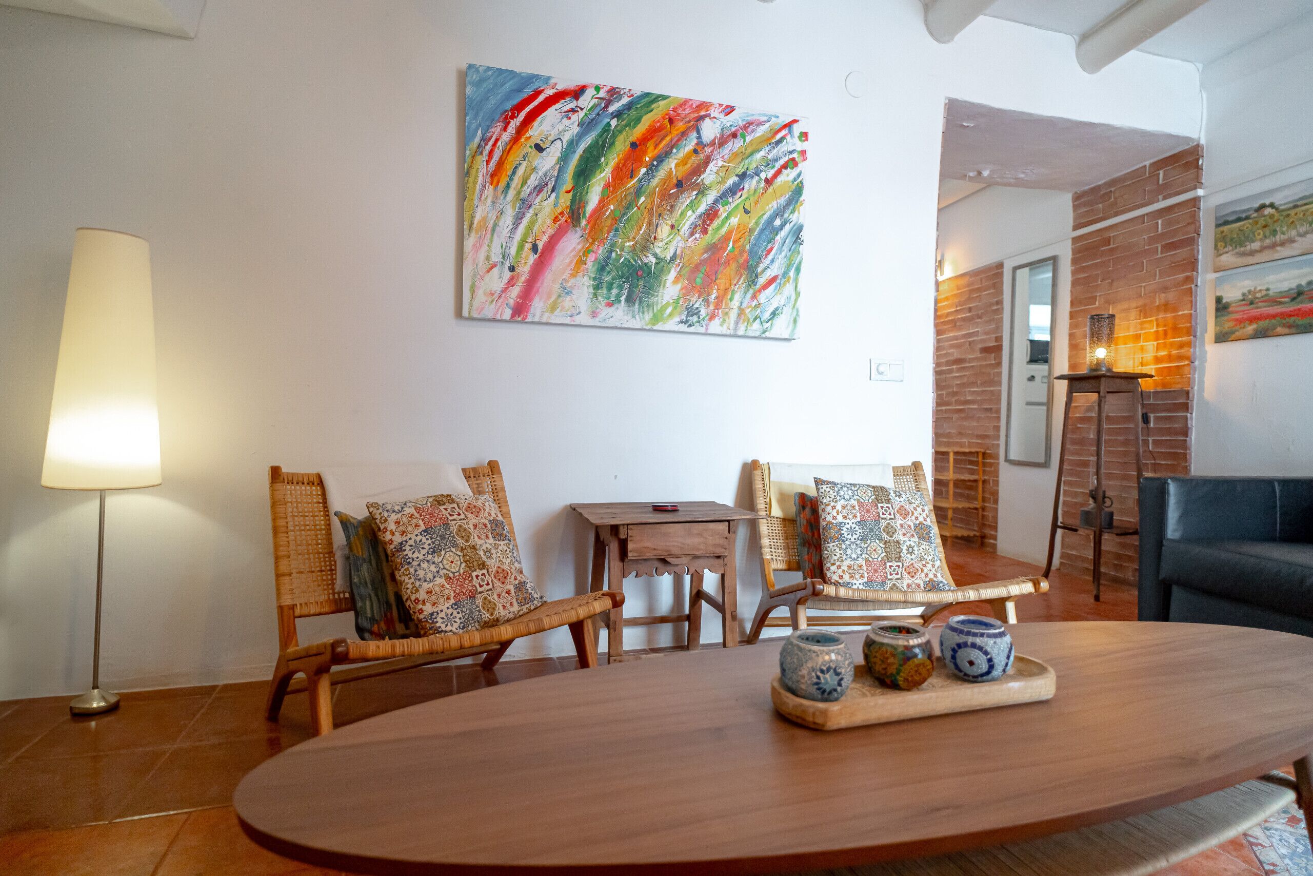 Un coin repas avec une table en bois, des chaises en osier et un tableau abstrait aux couleurs vives accroché au mur.