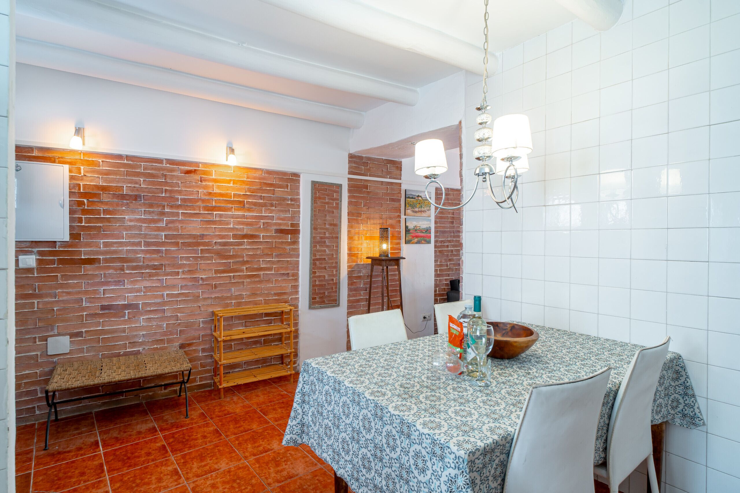 A dining area with a brick wall, white tiled walls, a wooden bench, and a table with chairs.