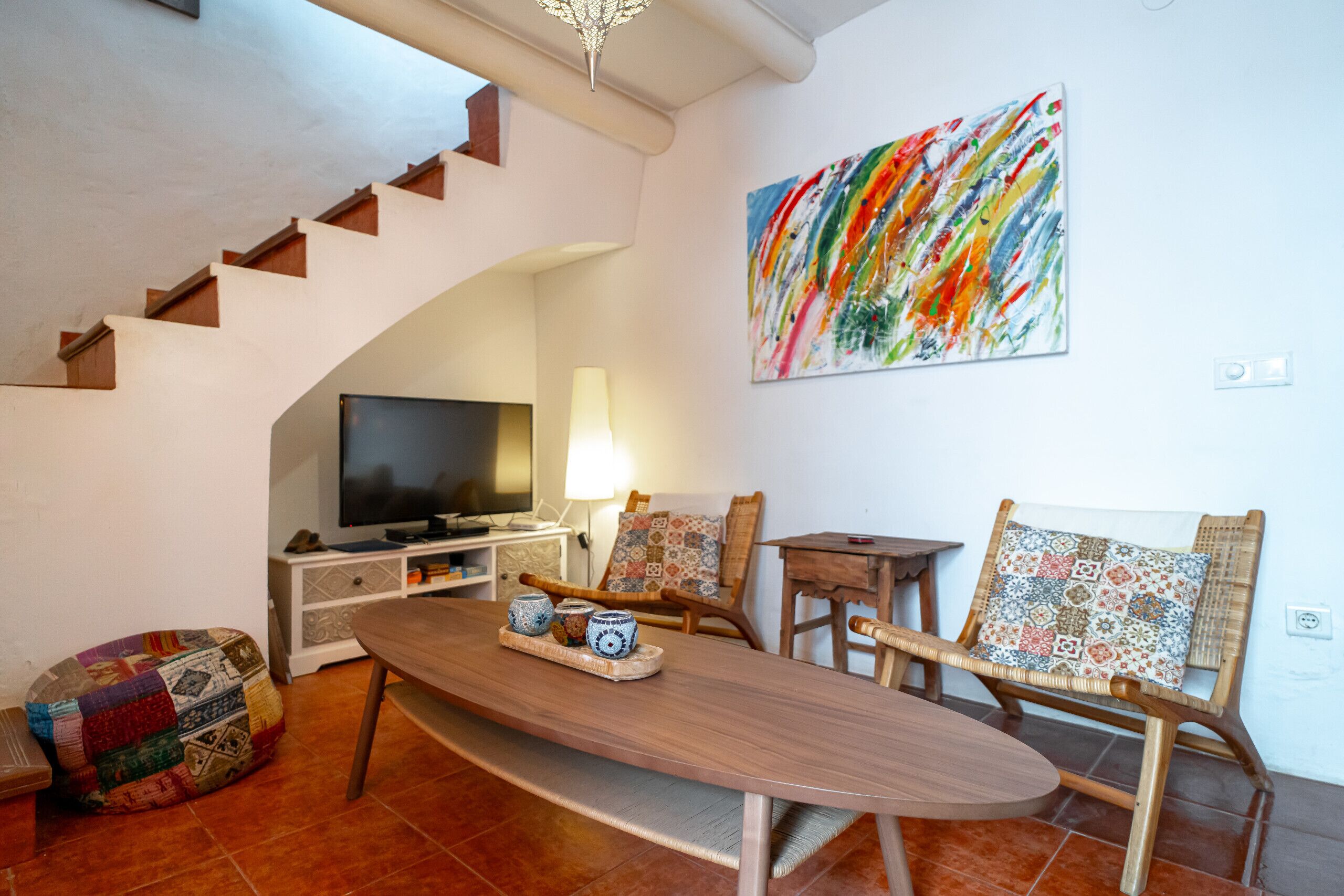 Un salon avec une table en bois, des chaises, un téléviseur et un tableau abstrait aux couleurs vives accroché au mur.