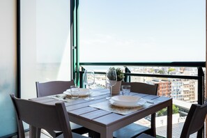 A dining table with chairs, a potted plant, and wine glasses set on a balcony with a city view. - Seasight Apartment by Wonderful Italy (Bari)