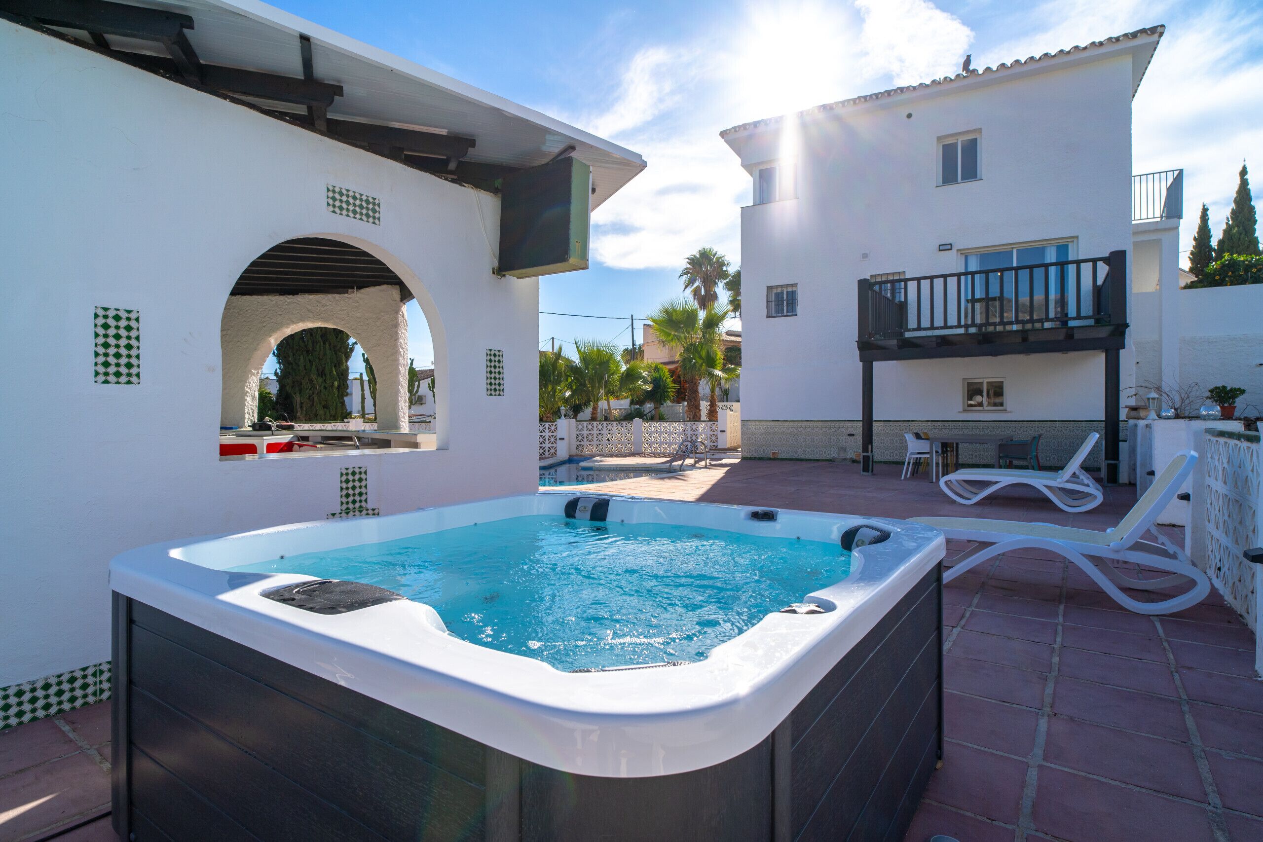 Un jacuzzi en un patio con piscina, sillas de descanso y un balcón.