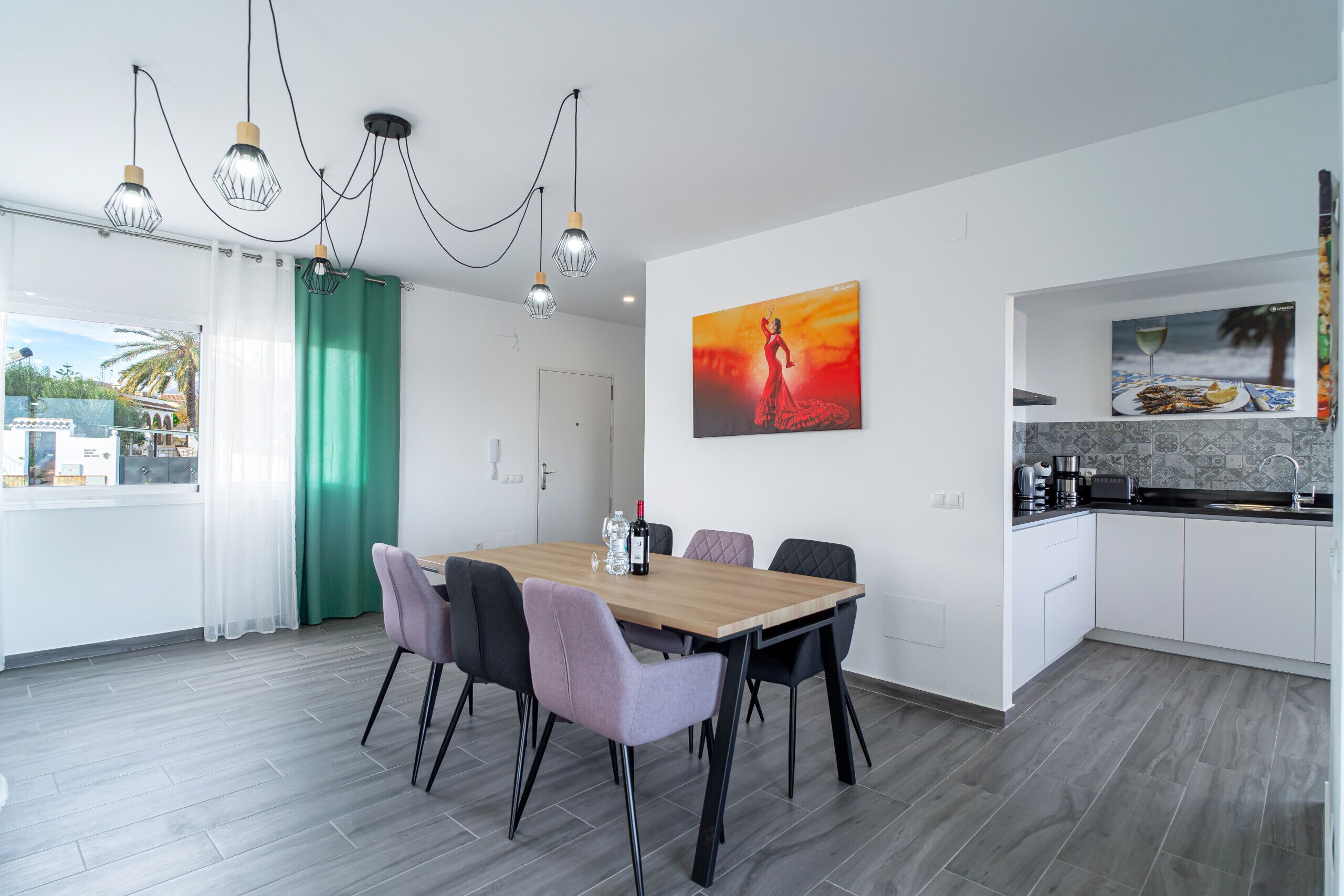 Eine moderne Küche mit Essbereich, ausgestattet mit einem Holztisch, Stühlen und Pendelleuchten.