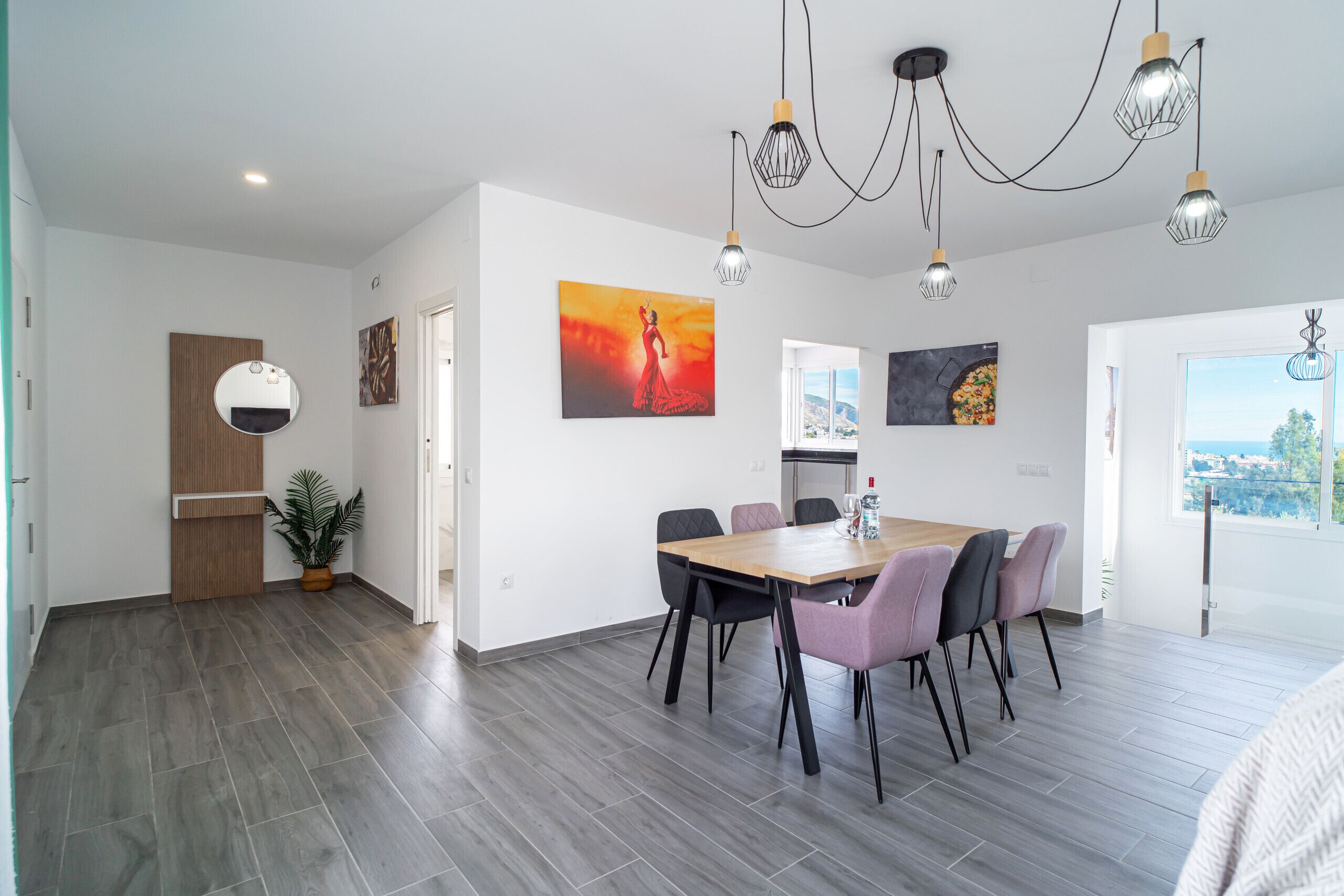 A modern dining area with a wooden table and chairs, a potted plant, and artwork on the walls.