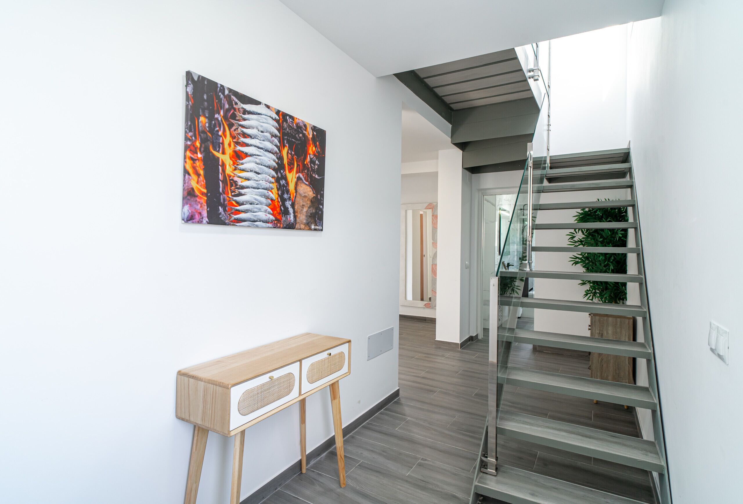 Een modern interieur met een trap, een houten console en een abstract schilderij aan de muur.