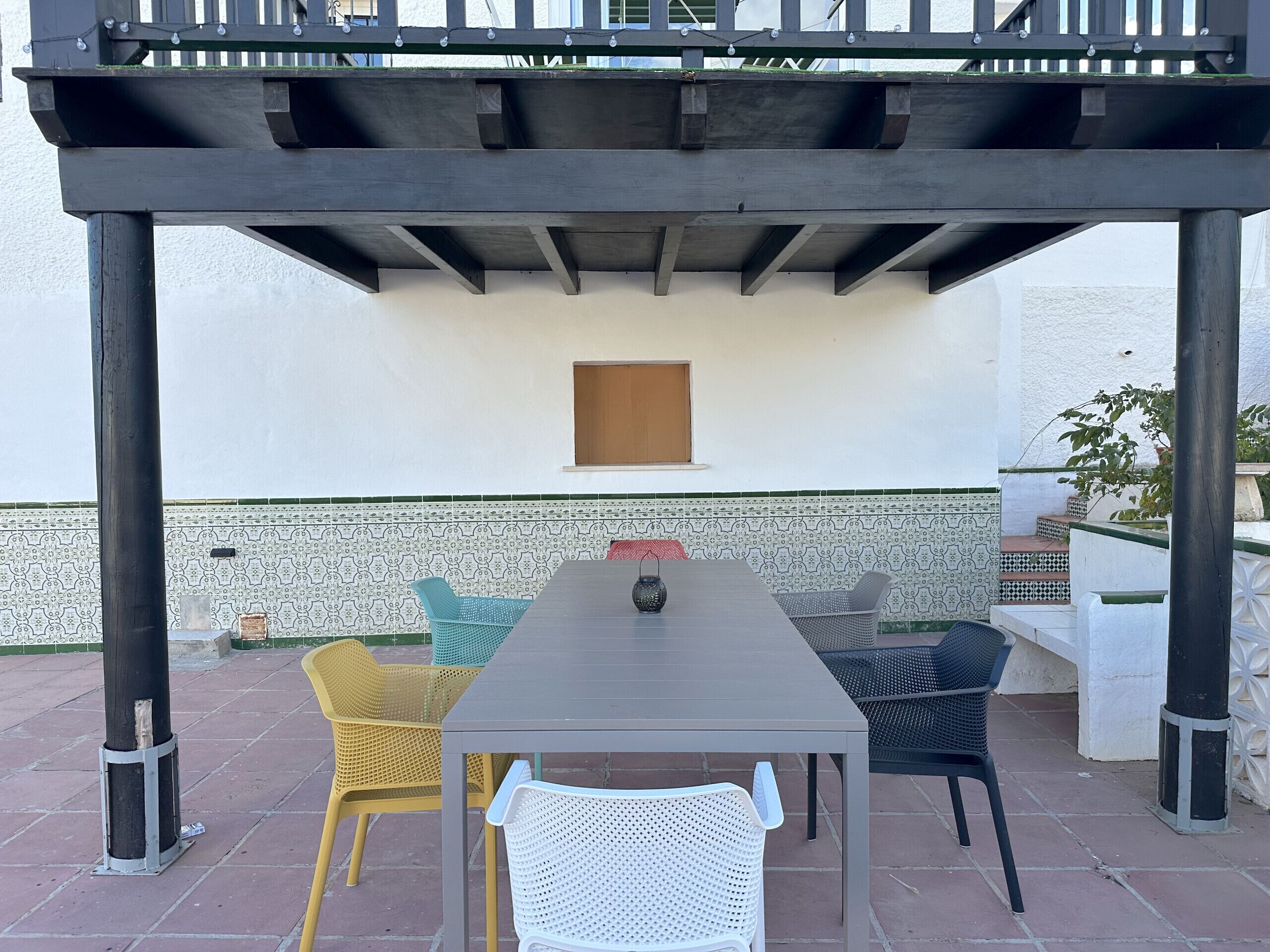 An outdoor patio with a table and chairs, a pergola overhead, and a patterned wall in the background.