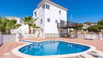 A white building with a pool, a balcony, and outdoor furniture.