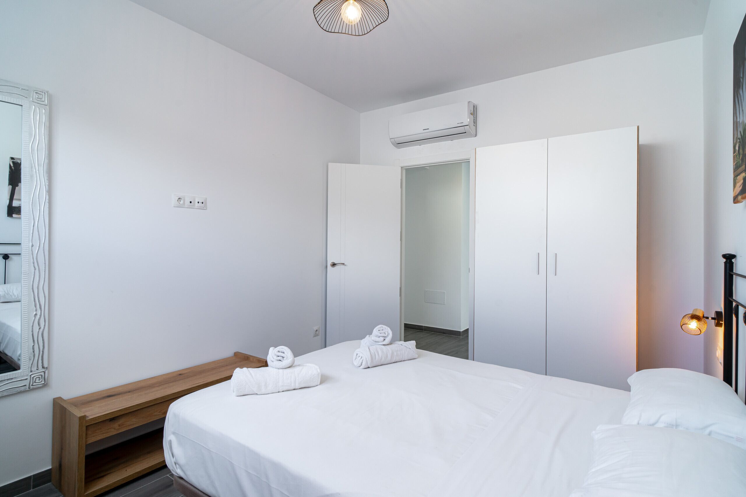 Una moderna camera d'albergo con un letto rifatto, una panca in legno, un armadio e un condizionatore d'aria.