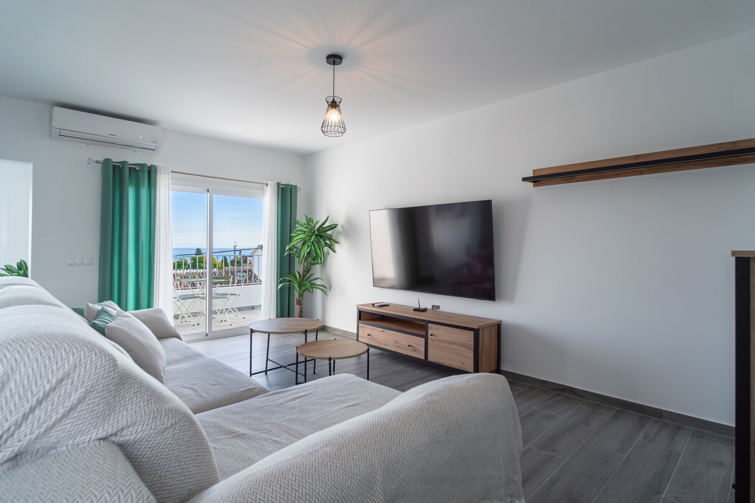 A modern living room with a sofa set, a flat-screen TV, a small table, and a potted plant.