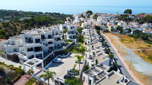 A modern residential area with white buildings, a parking area, and a view of the sea. - Royal Palm Luxe by Casasol (Nerja)