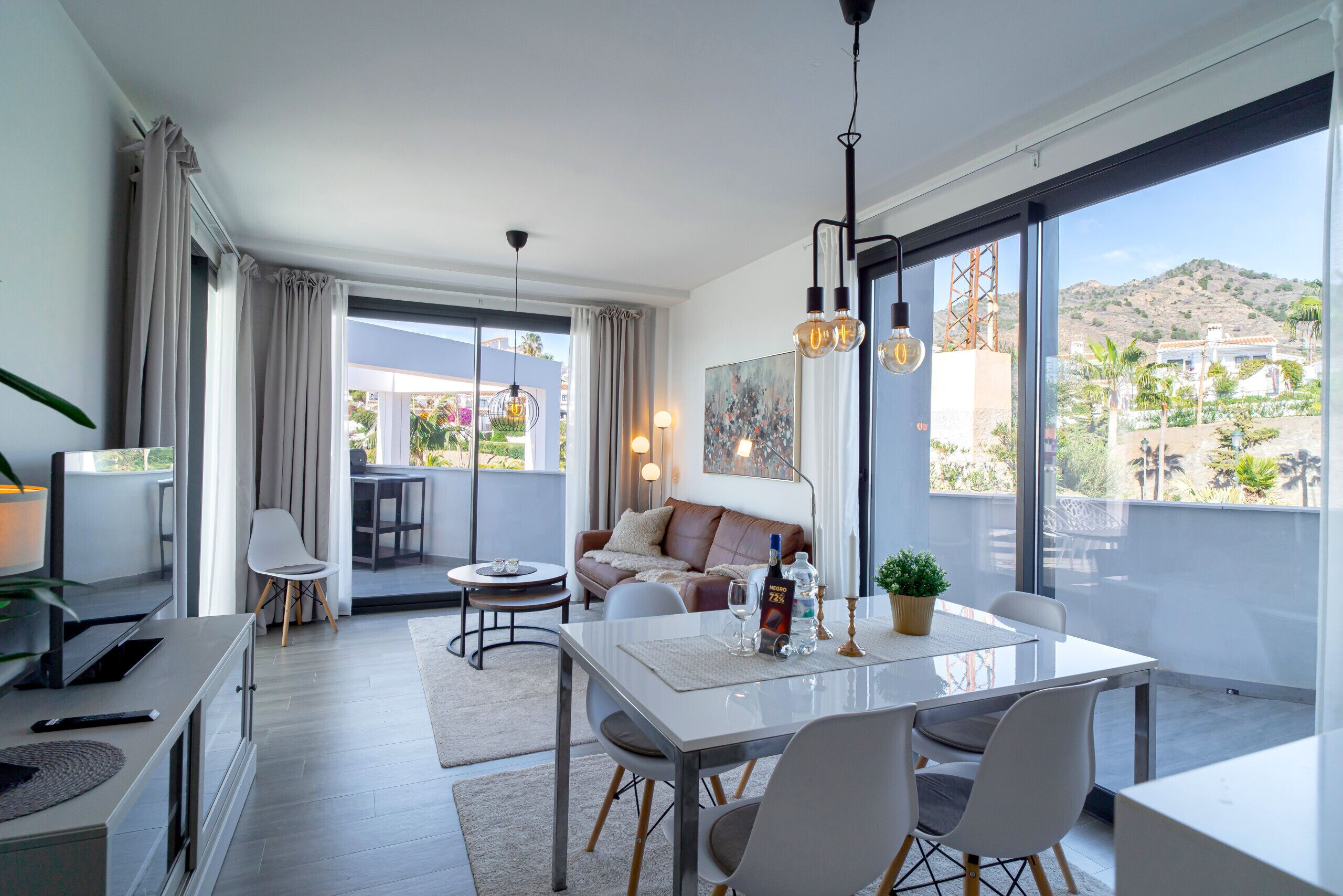 A modern living room with a dining area, large windows, and a view of the outdoors.