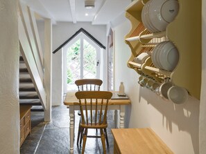 A dining area with a wooden table and chair, a wall-mounted dish rack, and a staircase leading to another room. - 1 bedroom accommodation in Wadebridge (Wadebridge)