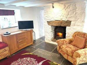 A cozy living room with a stone fireplace, a television on a wooden cabinet, and patterned furniture. - 1 bedroom accommodation in Wadebridge (Wadebridge)