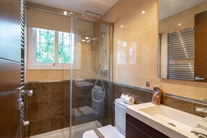 Een moderne badkamer met een douche met glazen wand, een witte wastafel en een handdoekhouder.