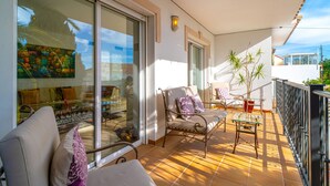 A balcony with a sofa, a chair, and a small table. There is a glass door leading to a room with a painting and a sofa. - Villa Grande Luxe Private Pool (Nerja)