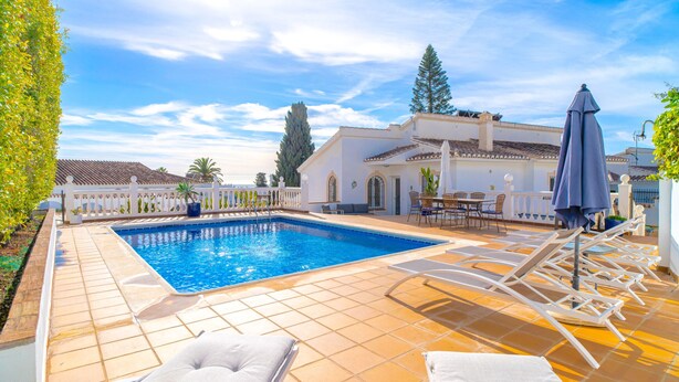 A swimming pool with lounge chairs and umbrellas, surrounded by a white fence and trees. - Villa Grande Luxe Private Pool (Nerja)