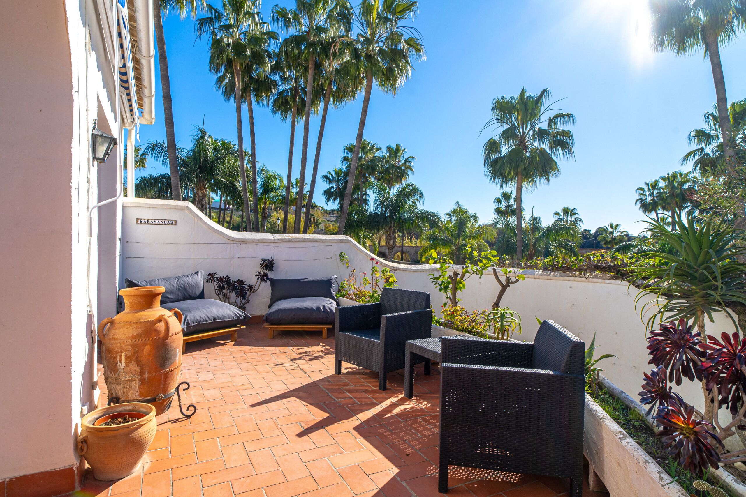 A patio with wicker furniture, a large terracotta pot, and a view of palm trees.