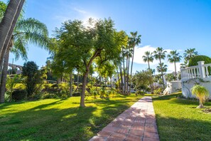 A pathway lined with palm trees and a white building with a balcony. - Casablanca Sunny Terrace by Casasol (Nerja)