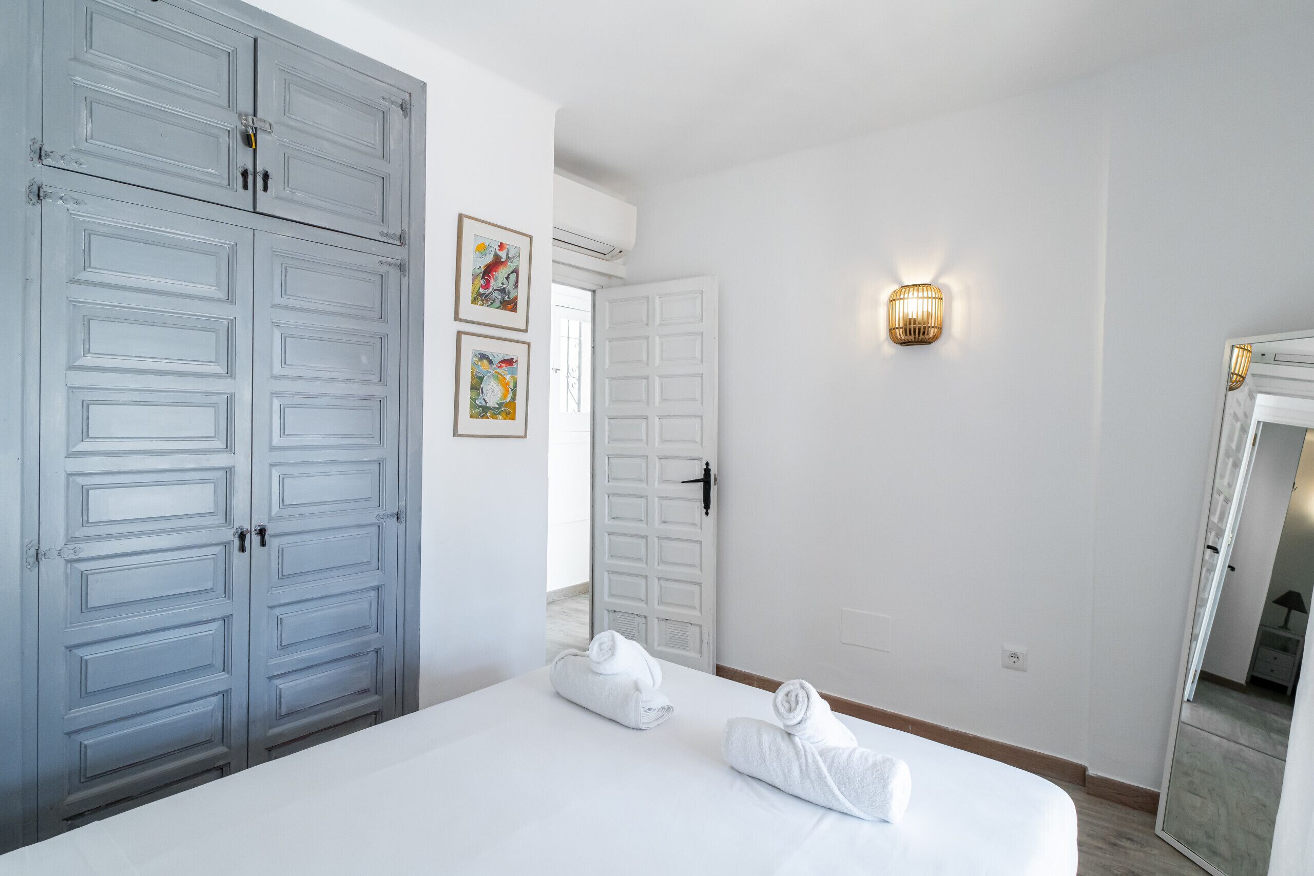 A hotel room with a large bed, a wardrobe, a wall-mounted light, and a door leading to another room.