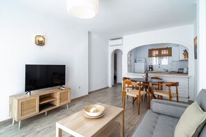 A modern living room with a flat-screen TV, wooden entertainment unit, and a dining area with a table and chairs. - Casablanca Sunny Terrace by Casasol (Nerja)
