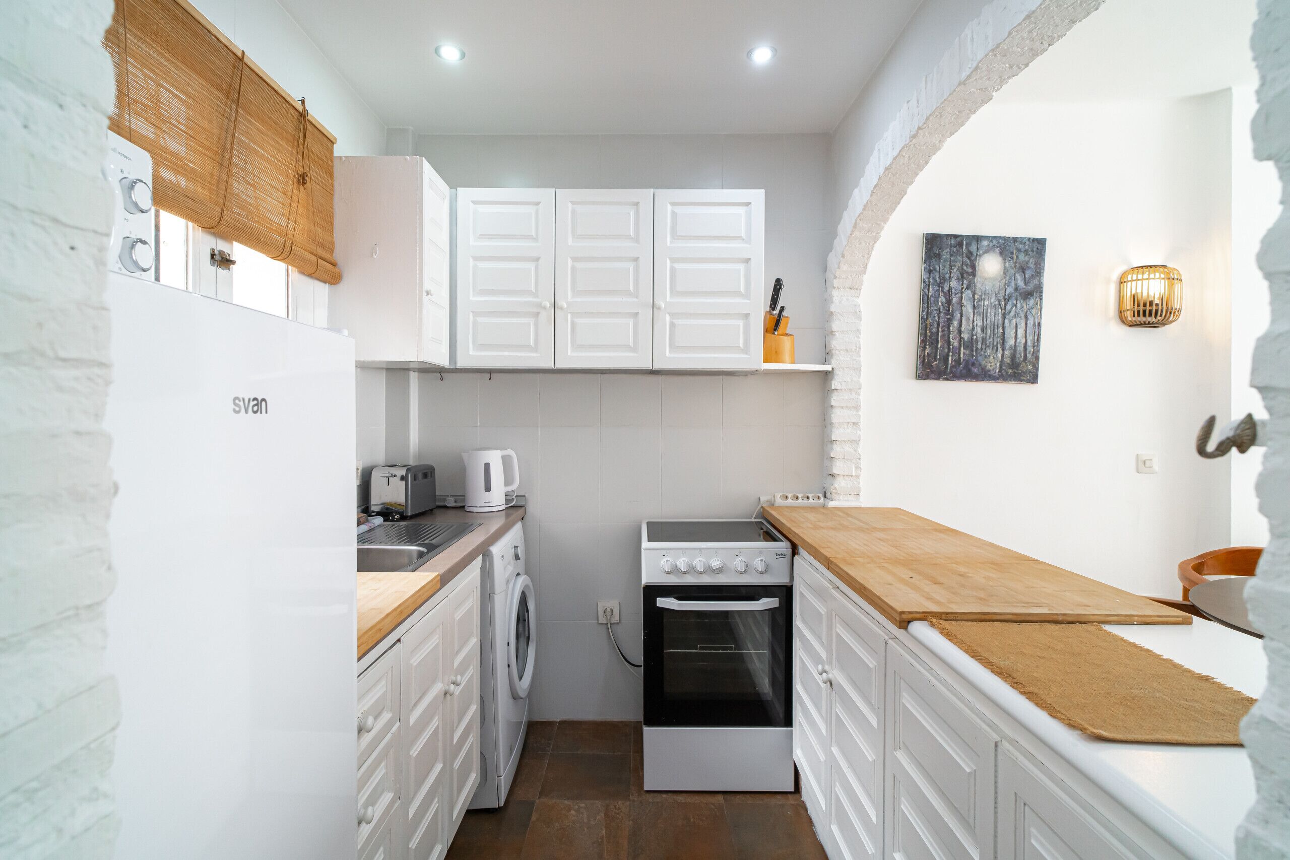 A compact kitchen with white cabinetry, a washing machine, a stove, and a microwave.