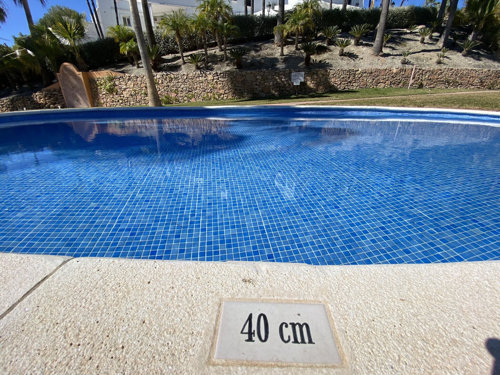 A swimming pool with a tiled blue surface, a stone wall, and a sign indicating a depth of 40 cm.