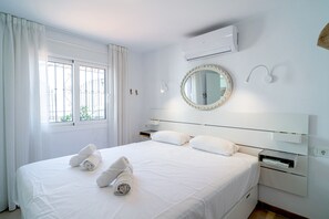 A neatly made bed with rolled towels, a bedside table, a mirror, and an air conditioning unit on the wall. - Casa Alegre by Casasol (Nerja)