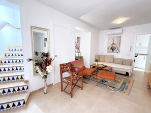 A modern living room with a sofa, a coffee table, and a chair. There is a staircase with colorful tiles and a mirror on the wall. - Casa Alegre by Casasol (Nerja)