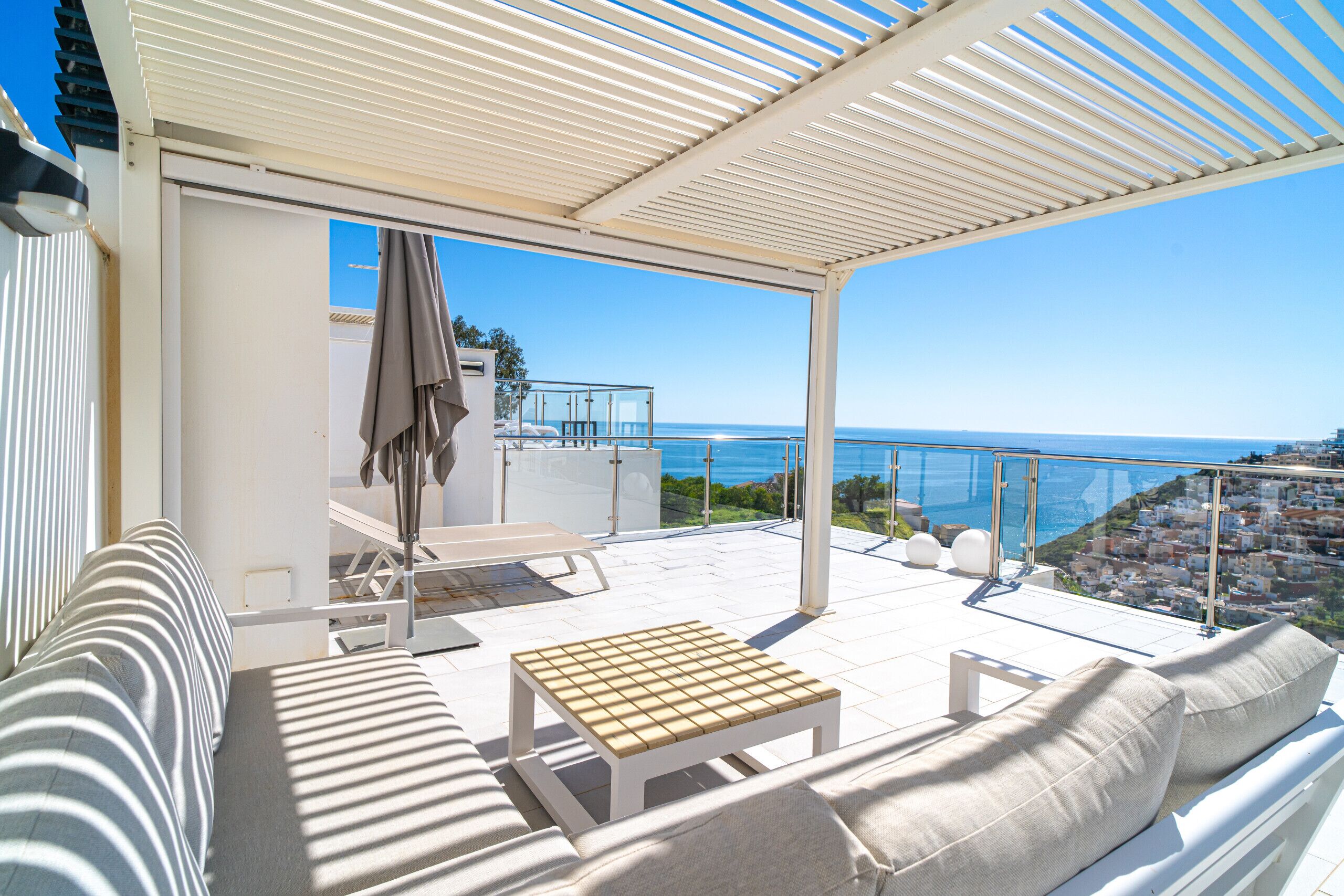A covered outdoor seating area with a view of the sea and a cityscape.