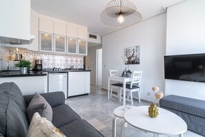 Eine moderne Küche mit weißen Schränken, ein Essbereich mit weißen Stühlen, ein graues Sofa und ein weißer Tisch mit einer Vase.
