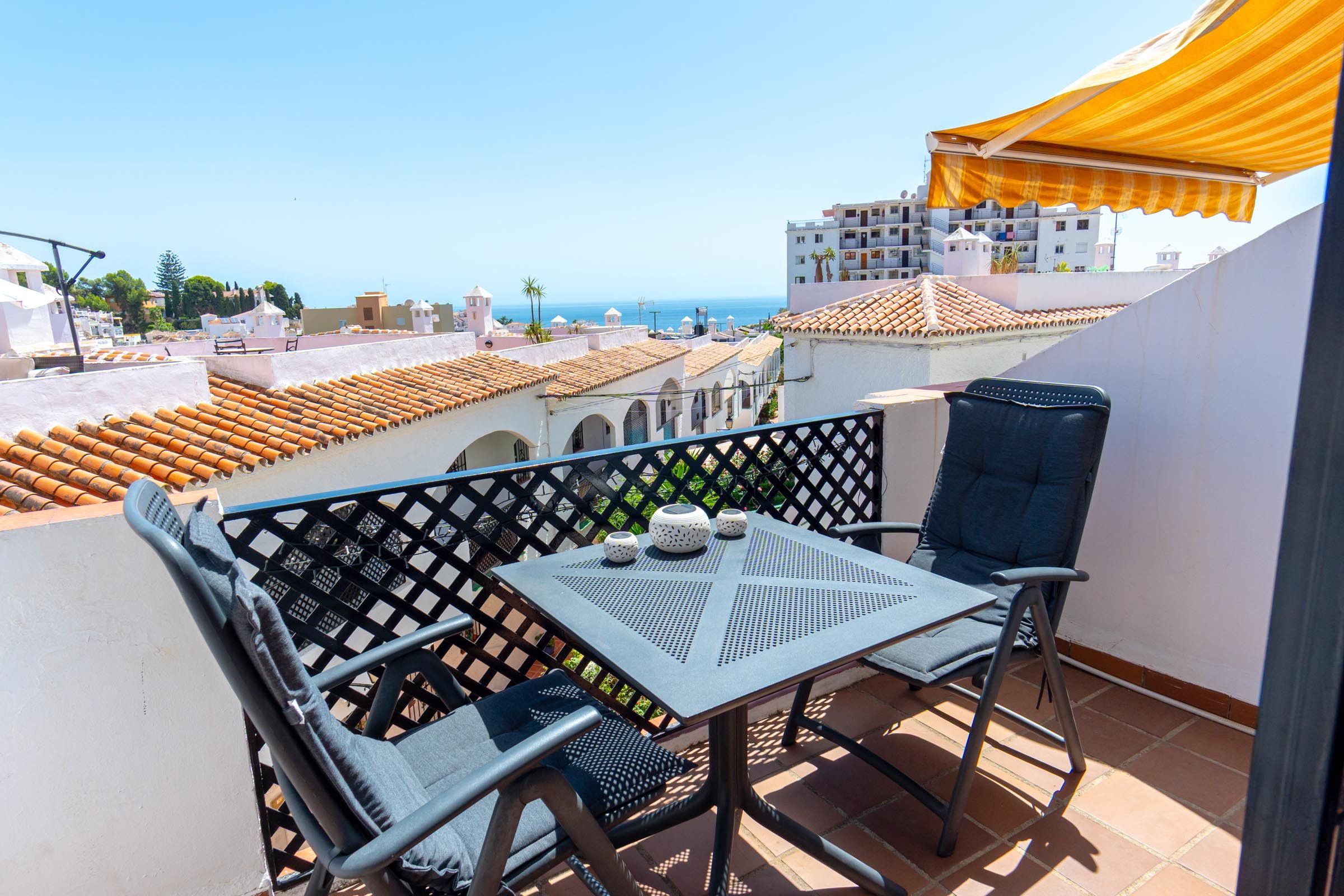 Ein Balkon mit Tisch und Stühlen, mit Blick auf eine Küstenstadt mit Terrakotta-Dächern.