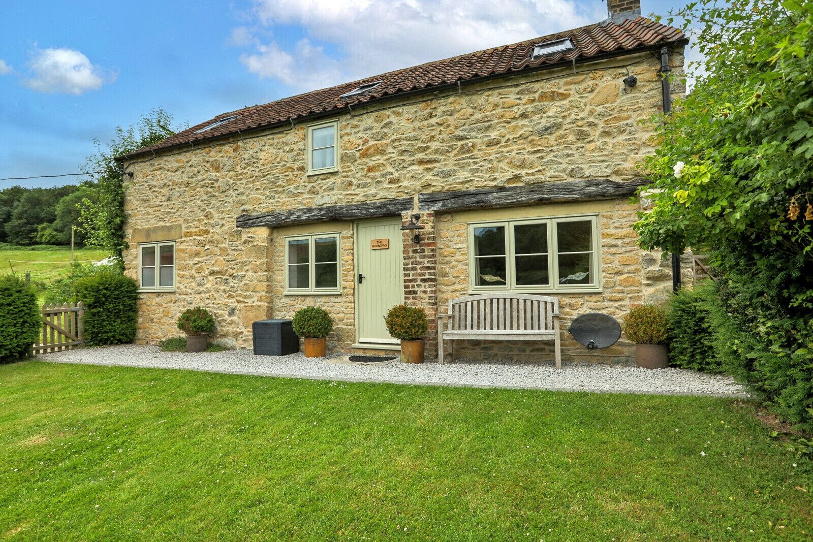 A stone house with a green door, a bench outside, and a gravel path leading to the entrance.