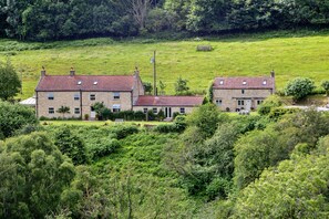 Ein Haus aus Stein mit Ziegeldach, umgeben von üppigem Grün und einer Wiese.