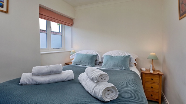 Ein Schlafzimmer mit einem Bett, zwei Nachttischen, einem Fenster mit Jalousie und einer Wandlampe.