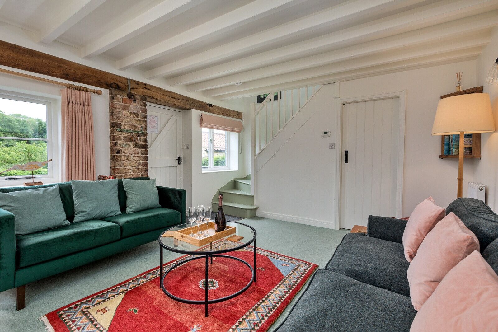 Un salon avec un canapé vert, un canapé gris, un tapis rouge et un escalier.