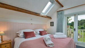 Ein Schlafzimmer mit Bett, Kissen, Nachttisch, Lampe, Fenster und Blick ins Freie.