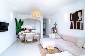 Ein modernes Wohnzimmer mit Sofa, einer Essecke mit Tisch und Stühlen sowie einer Küche im Hintergrund.
