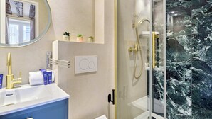 Een badkamer met een marmeren douche, een ronde spiegel en een blauwe wastafel.