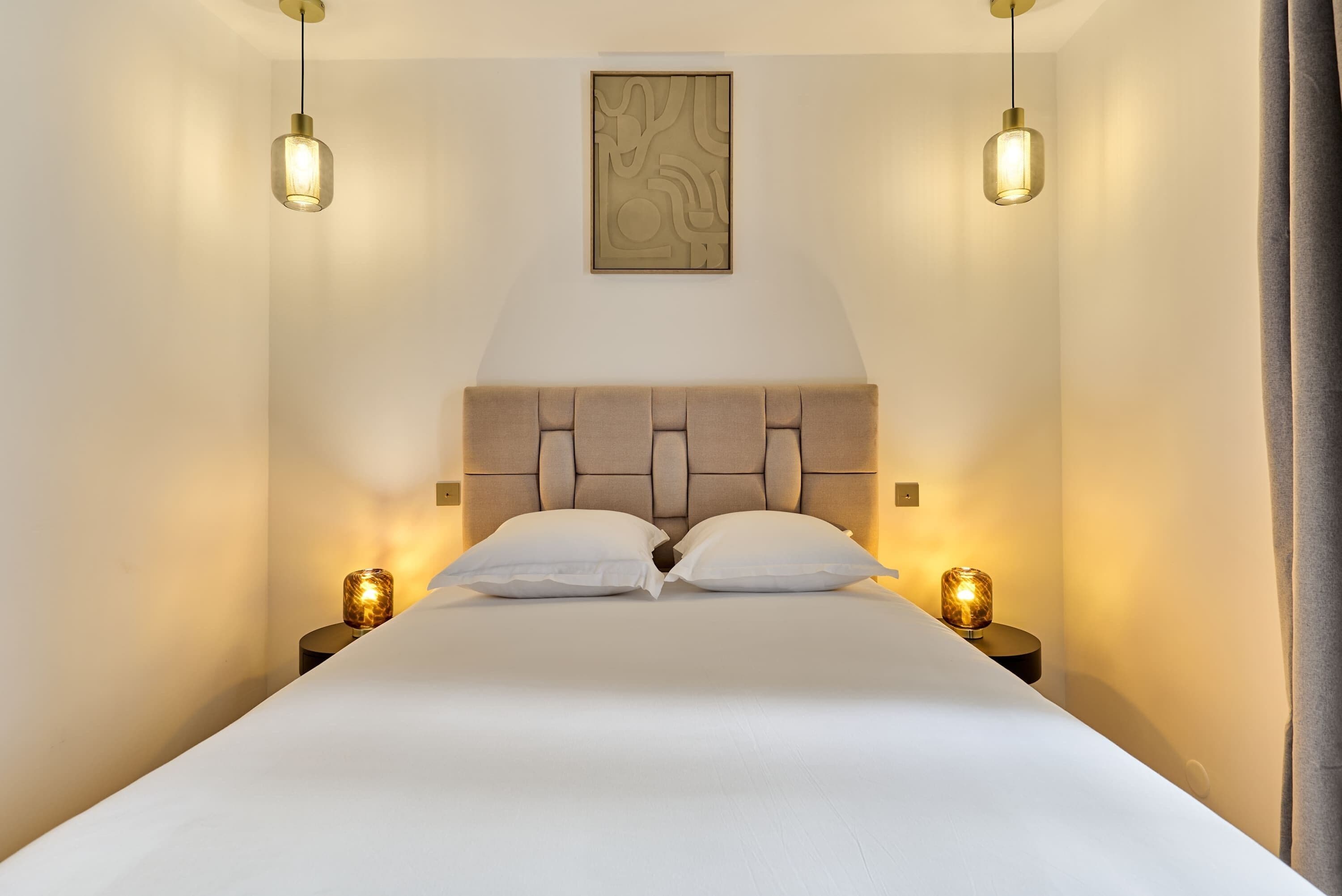 Een bed met hoofdeinde, twee bedlampen en een kunstwerk aan de muur.
