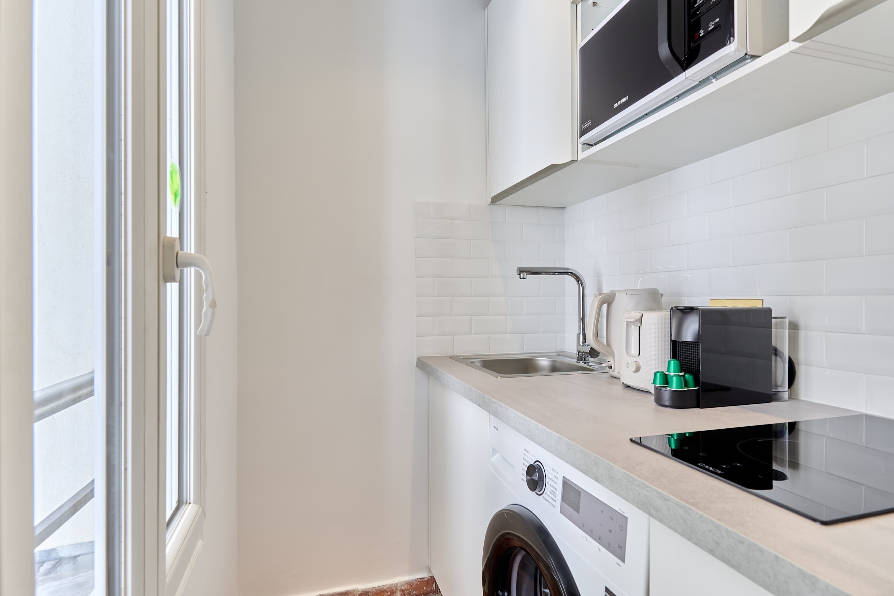 Une cuisine compacte équipée d’un lave-linge, d’une machine à café et d’un four à micro-ondes.