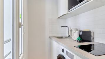 Een compacte keuken met een wasmachine, koffiezetapparaat en magnetron.