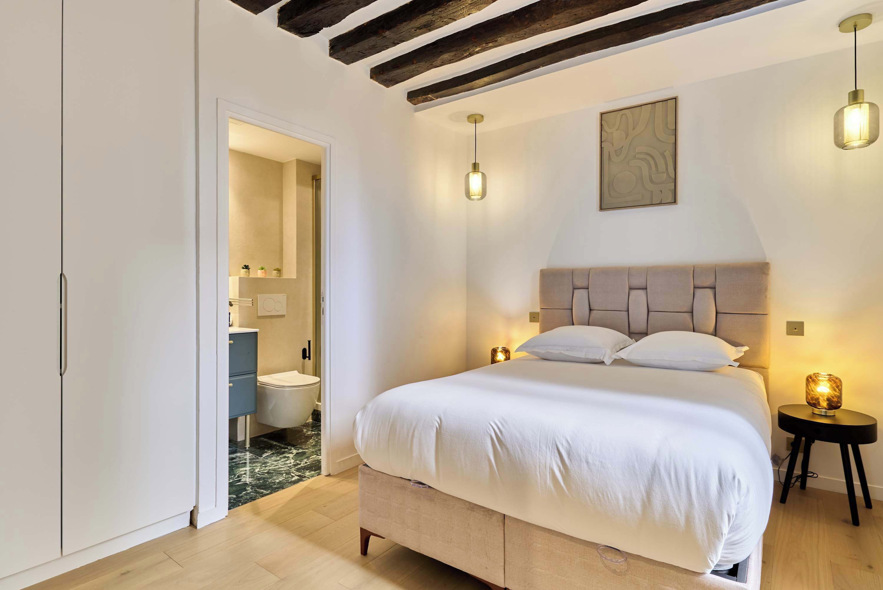A bedroom with a bed, bedside lamps, a headboard, and a door leading to a bathroom.