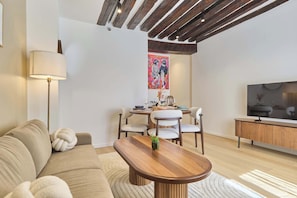 A modern living room with a sofa, a wooden coffee table, a dining table with chairs, a lamp, and a painting on the wall. - Charming apartment in Le Marais Center of Paris (Paris)