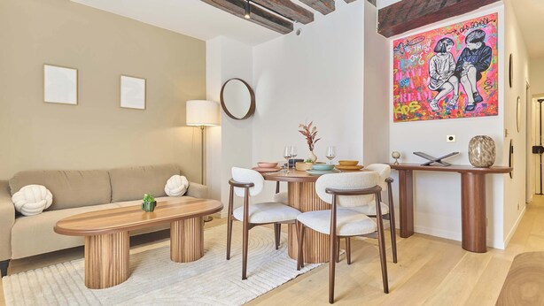 Een woonkamer met een bank, salontafel, stoelen, een eettafel en een schilderij aan de muur.