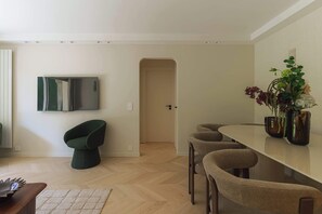A modern dining area with a wooden table, several chairs, a green chair, and a wall-mounted TV. - Apartment & Private Garden - Deauville-Sévigné (Deauville)