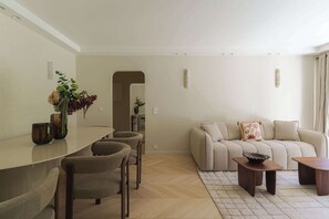 A modern living room with a sofa, coffee table, and chairs. There is a dining area with a table and chairs. - Apartment & Private Garden - Deauville-Sévigné (Deauville)